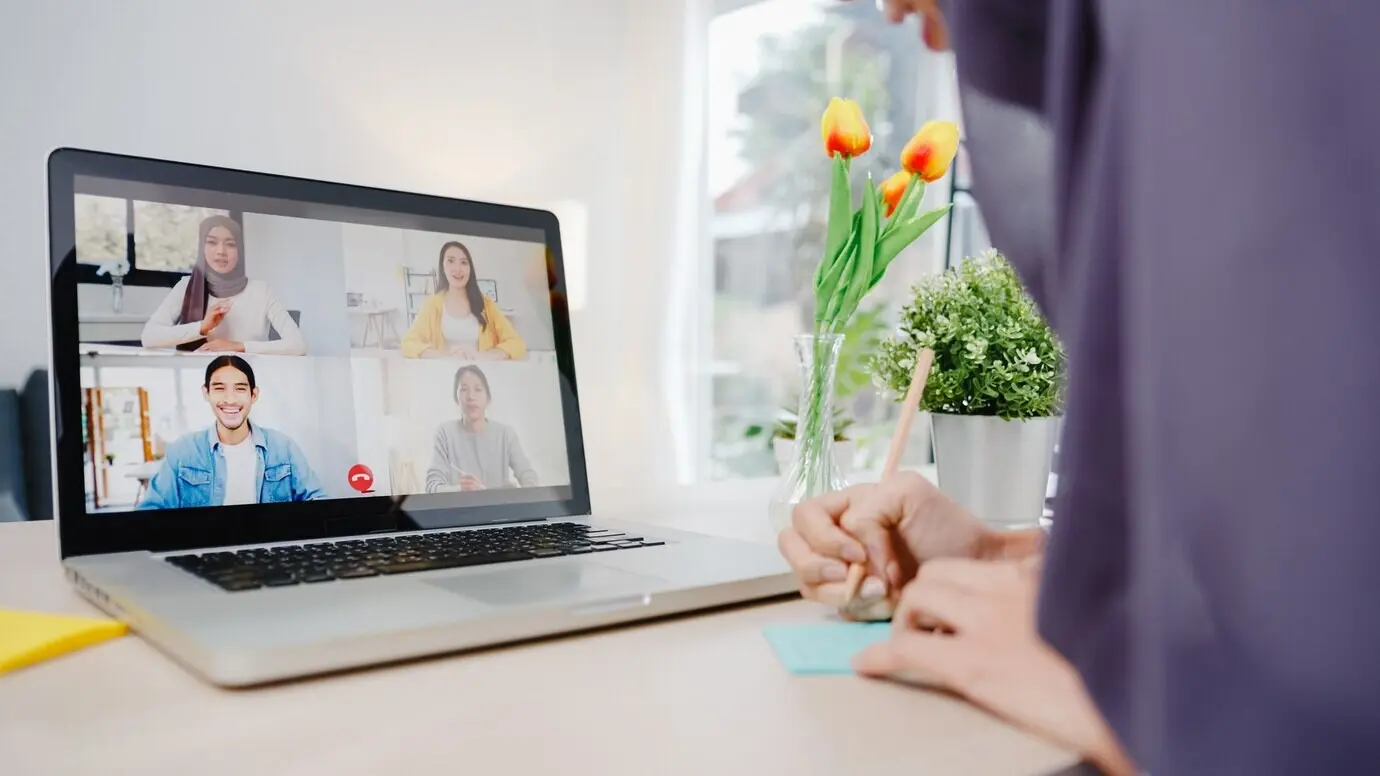 Предпринимательница-мусульманка, работая удалённо из дома в гостиной, по видеосвязи через ноутбук обсуждает с коллегой план на онлайн-встрече в формате мозгового штурма.