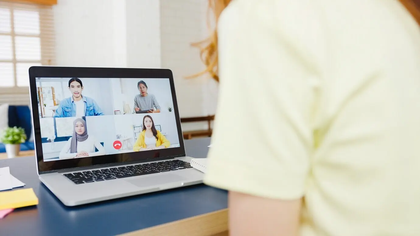 Бизнес-леди из Азии использует ноутбук, чтобы на видеовстрече обсудить с коллегами план, работая из дома в гостиной. Самоизоляция, социальное дистанцирование, карантин для профилактики коронавируса.