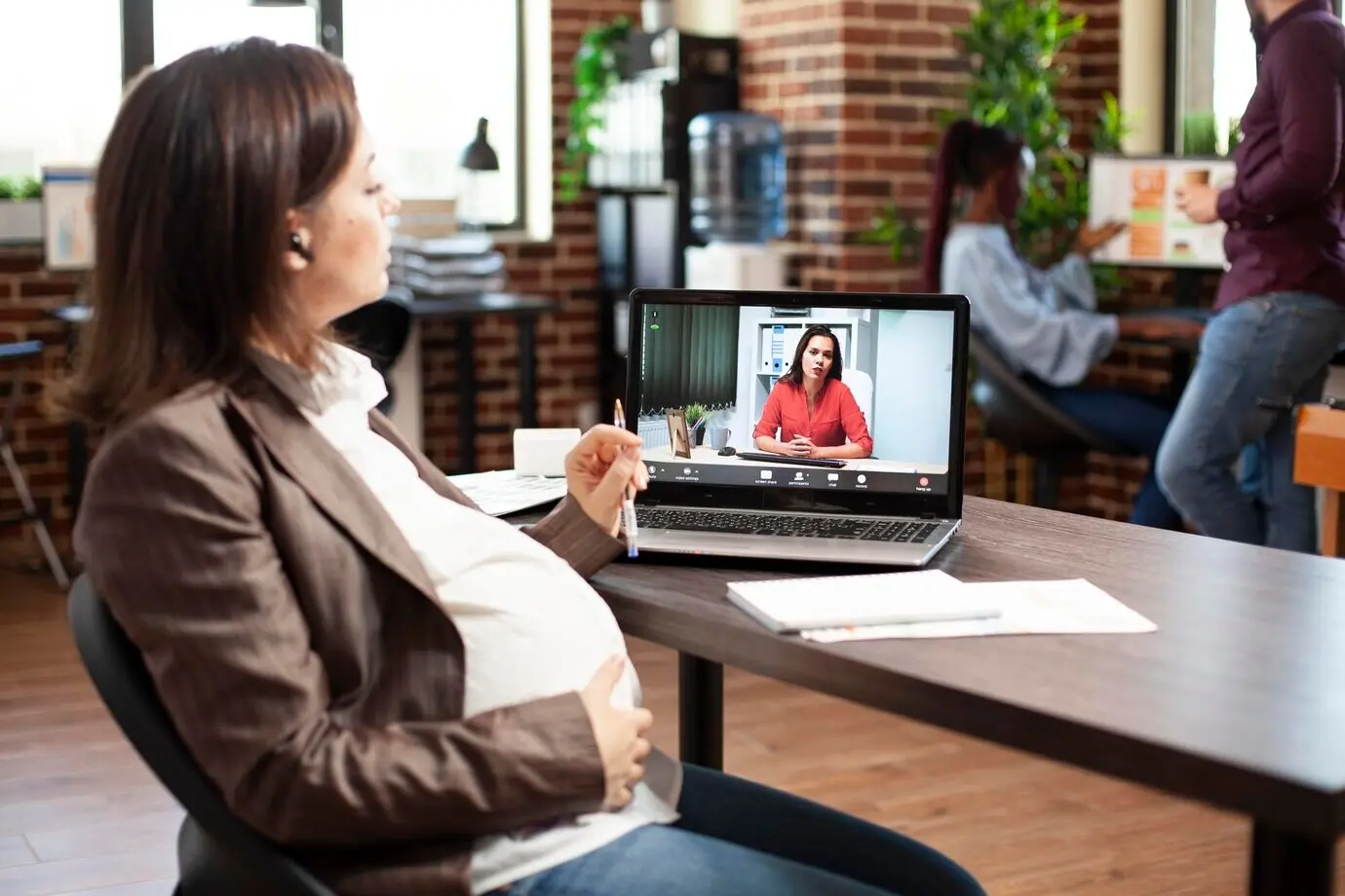 Беременная женщина ведет видеозвонок с ноутбука.